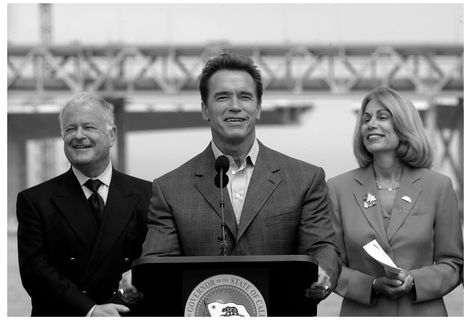 Figure 8.3. Governor Schwarzenegger signing funding legislation with California Senator Don Perata on the left and Secretary Sunne McPeak of Business, Housing and Transportation Agency on the right; original Bay Bridge in background, 2005.