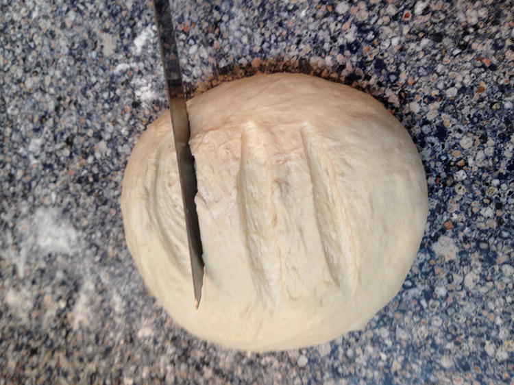 Photo of a knife slightly slicing the surface of a growing dough.