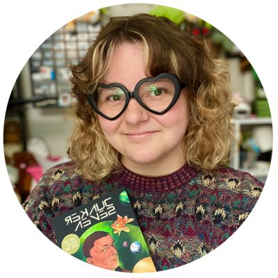 A picture of Olive J. Kelley, a green-haired nonbinary person, smiling and holding a white cat.