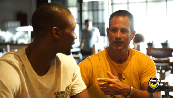 A color photograph depicting two men, Sam (right) and Chris Bosh (left), conversing with each other and Sam pointing a finger toward Chris