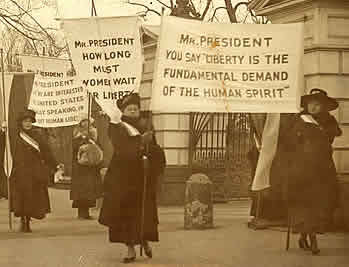 Four women hold signs addressed to the president demanding liberty for women. One banner reads, Mr President, You say Liberty is the  Fundamental Demand of the Human Spirit. Another banner reads, Mr President, how long must women wait for liberty. 