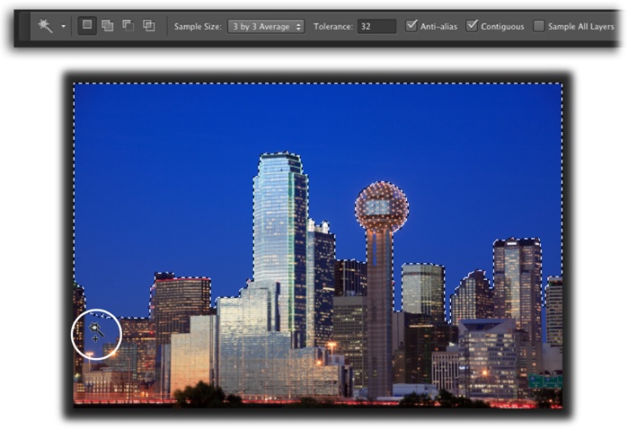 With its tolerance set to 32, the Magic Wand did a good job of selecting the sky behind downtown Dallas.You’ve got several ways to select the spots it missed, like the area circled at the bottom left: You can add to the selection by pressing the Shift key as you click in that area; increase the Tolerance setting in the Options bar and then click the sky again to create a brand-new selection; or flip to page 151 to learn how to expand the selection with the Grow and Similar commands.