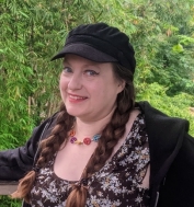 A person with braids wearing a hat and a black jacket

Description automatically generated