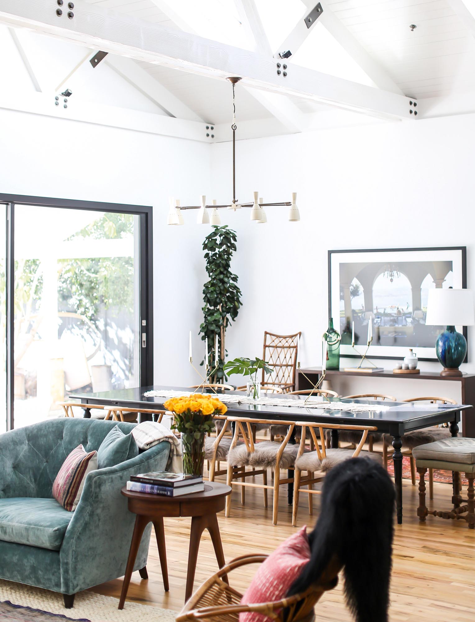 A traditional table with curated chairs for twelve are positioned under a contemporary sconce chandelier in an open dining and living area.