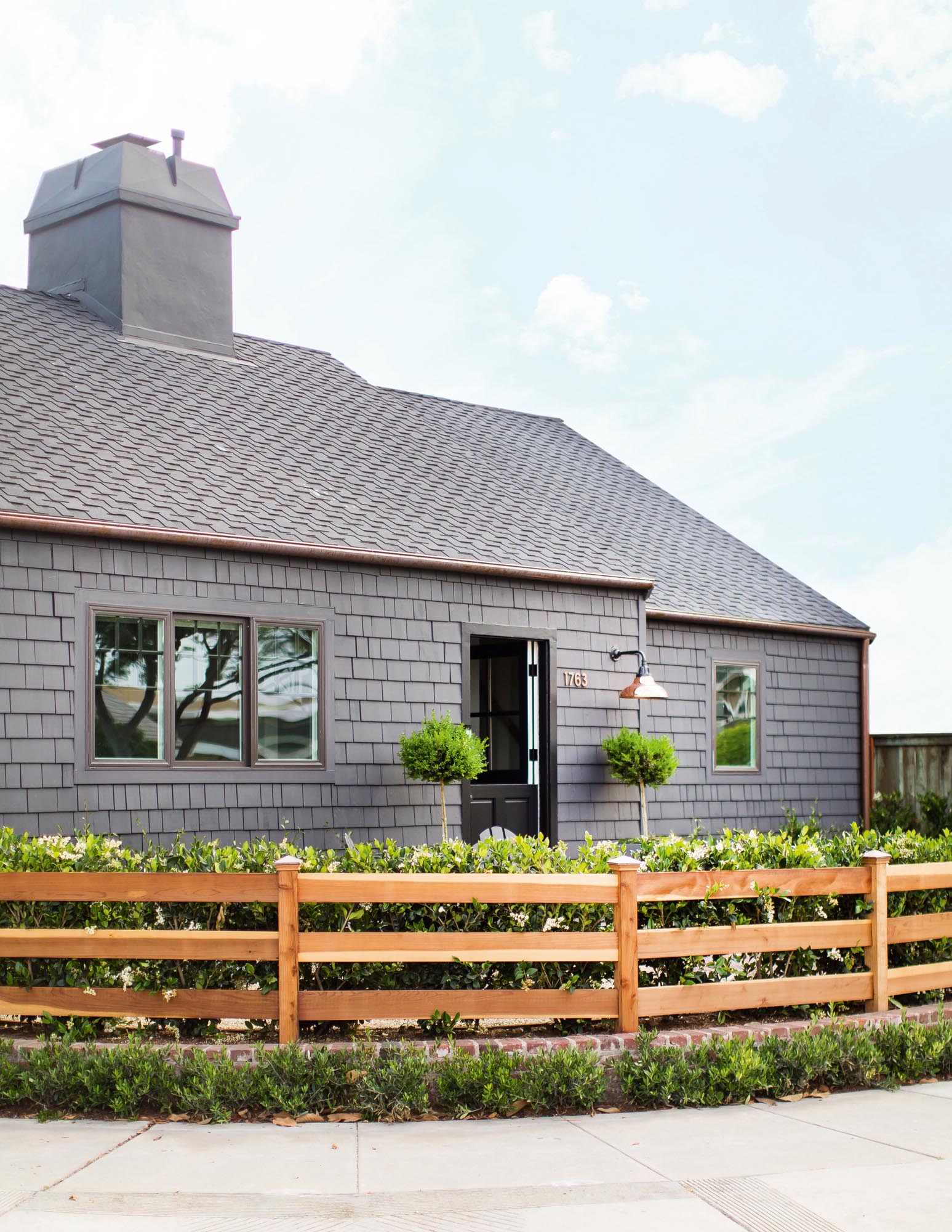 Photo of the exterior of a cabin covered in gray shingles and surrounded by a low natural wood fence.