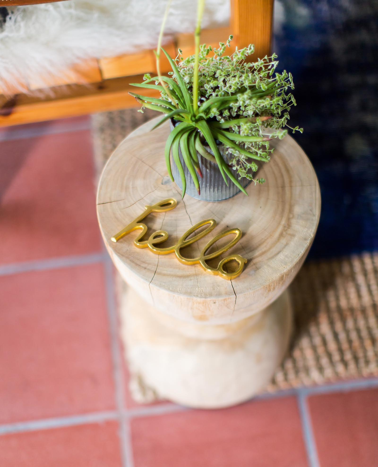 Photo of a side table made from a single piece of natural wood, topped with a plant and the word "hello" made of metal.