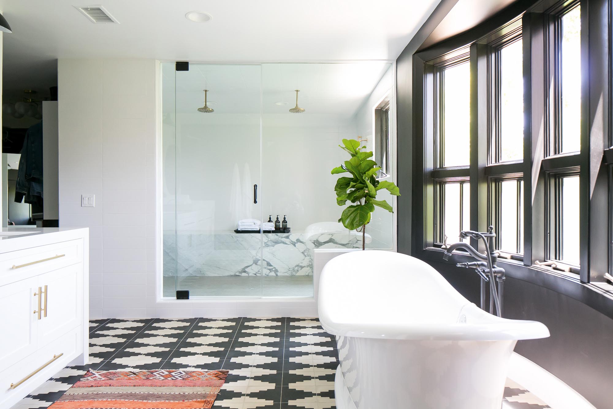 The en suite master bathroom is a symphony of Rorschach-patterned black-and-white tile with a double-headed French shower on one end of the room and a French bateau pedestal tub on the other.