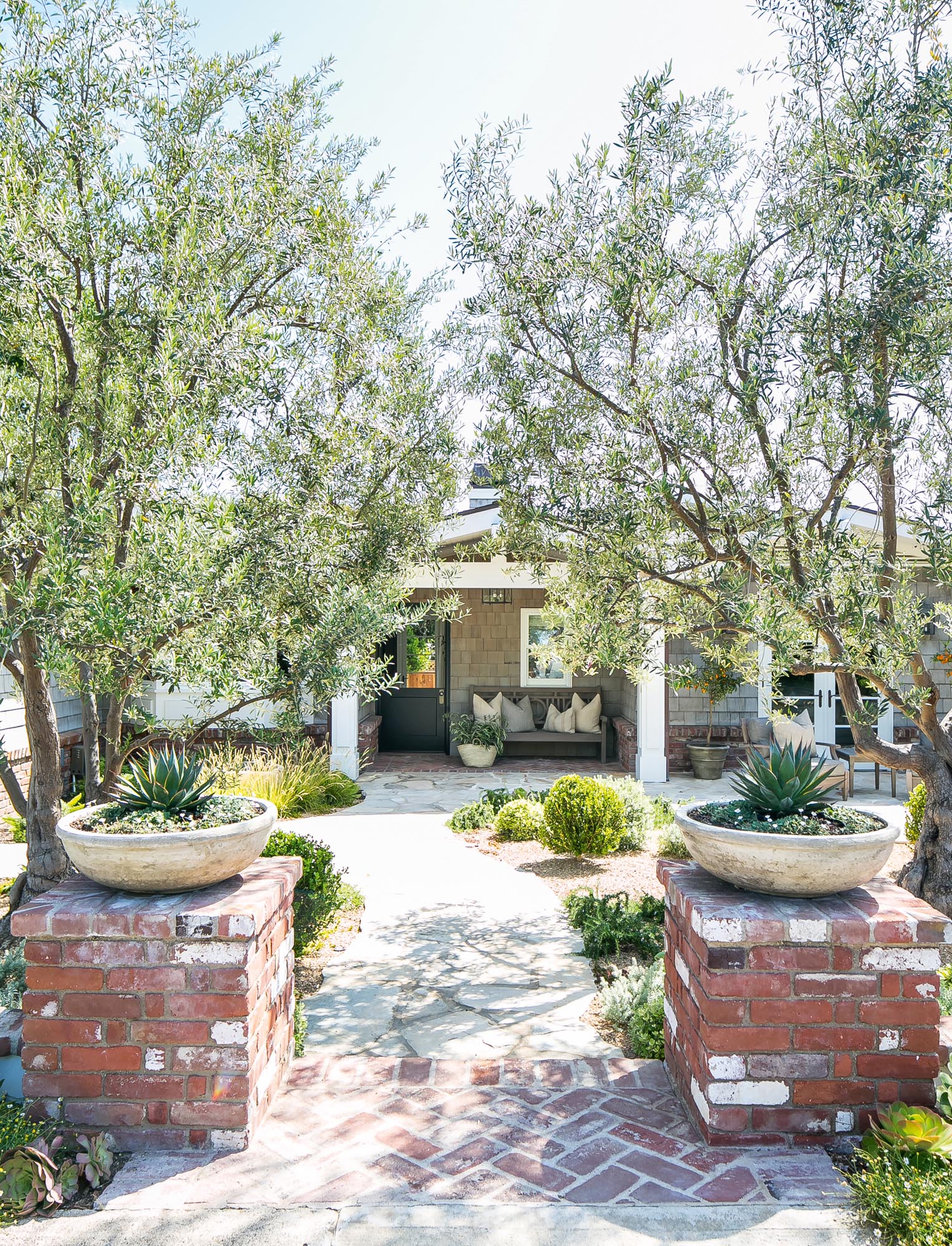 Photo of low brick pillars in front of twin trees flank the entry to the front path.