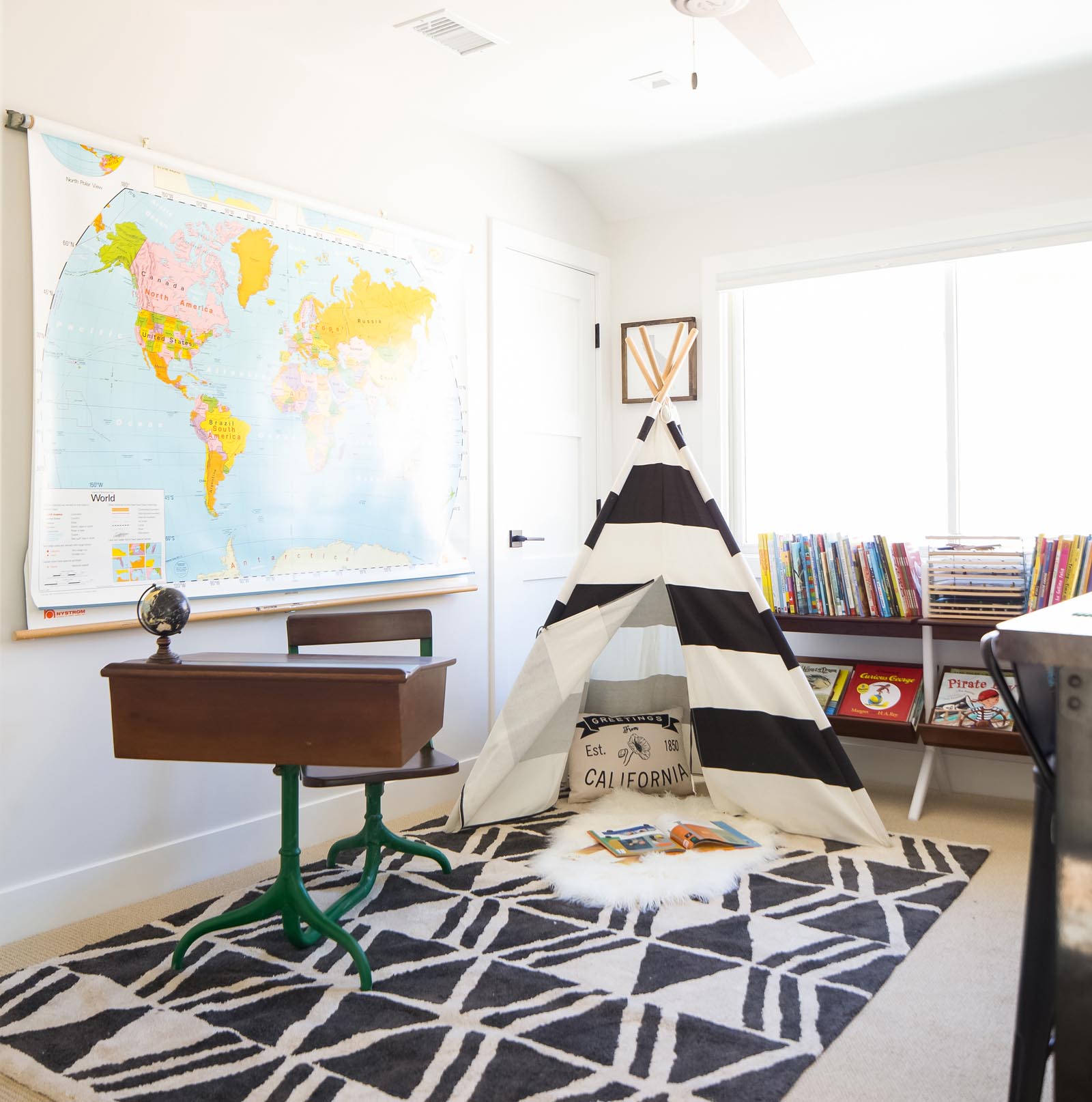 Photo of a student desk, large maps on the wall, the tepee, and a bookcase full of picture books and puzzles.