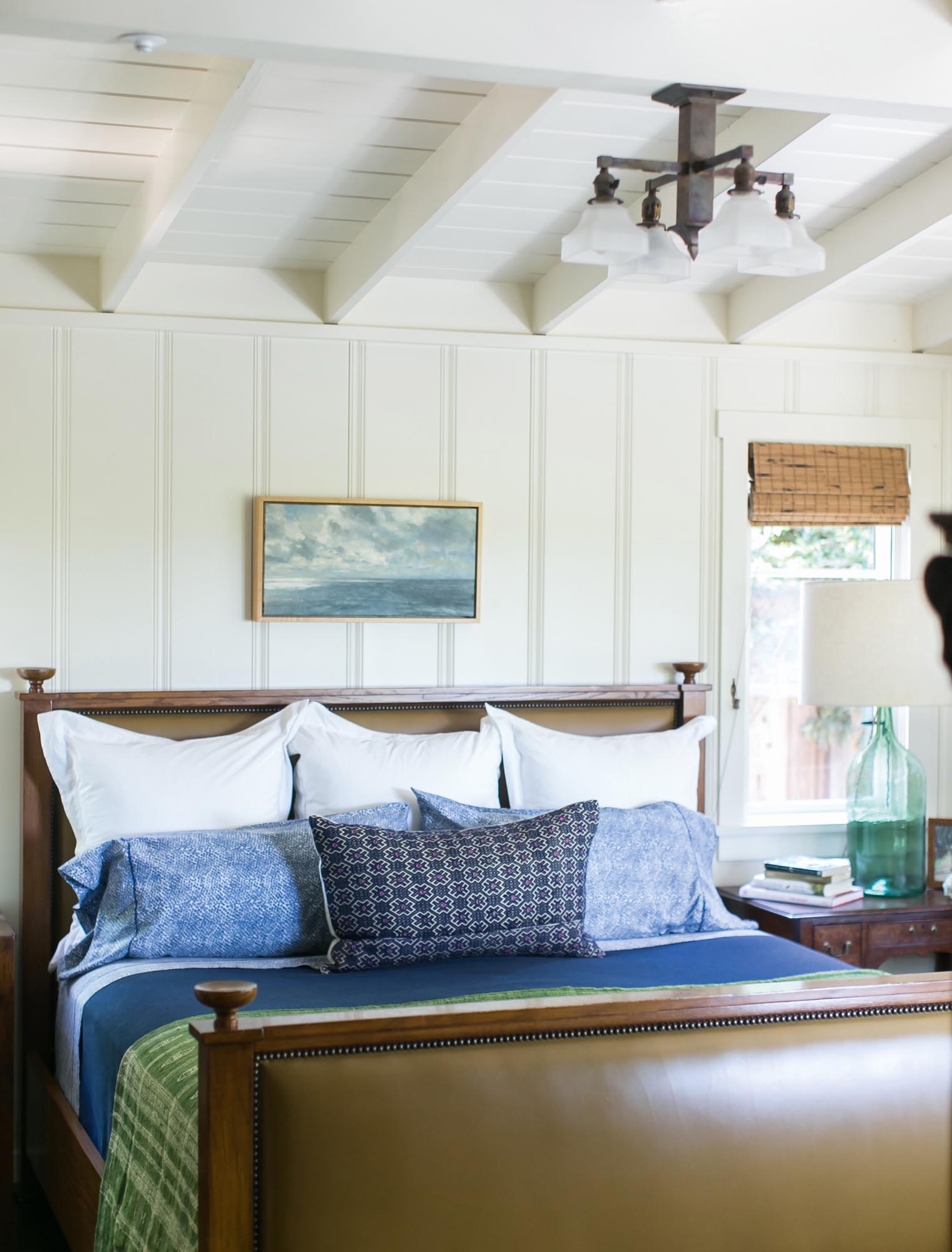 The master bedroom with its vintage English leather headboard and matching footboard is accented with Indigo custom lumbar pillows, a 1920s inspired fixture and one of many notable vintage paintings found throughout the cottage.