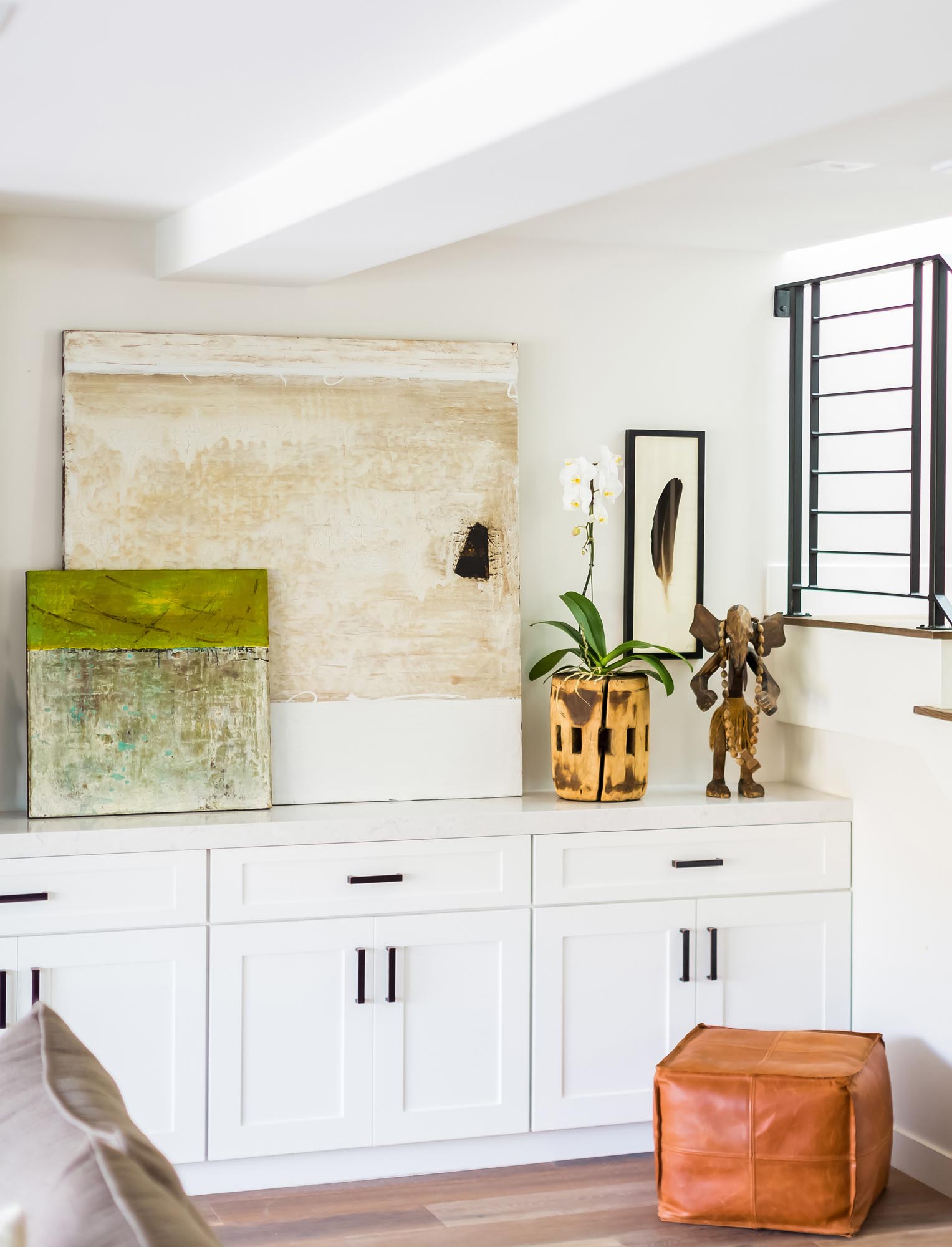 Photo of paintings and a potted flower above more white cupboards.