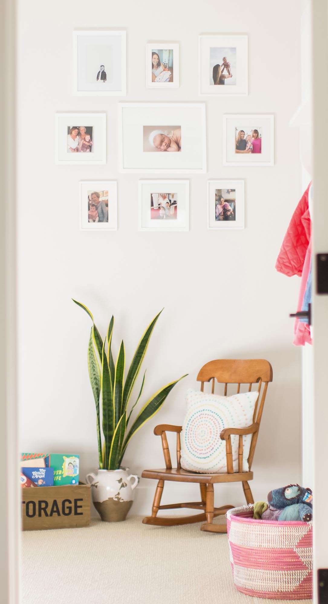 Photo of a small rocking chair under a collage wall of baby pictures.