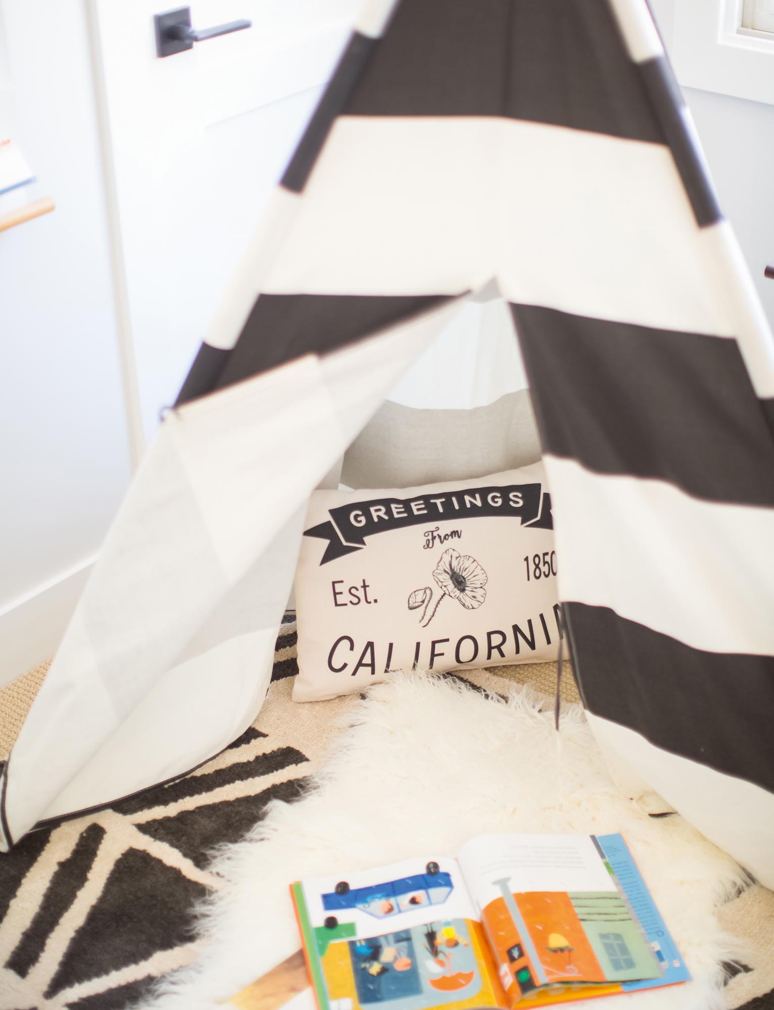 Photo of a child-size tepee, cozy rugs, and a picture book.