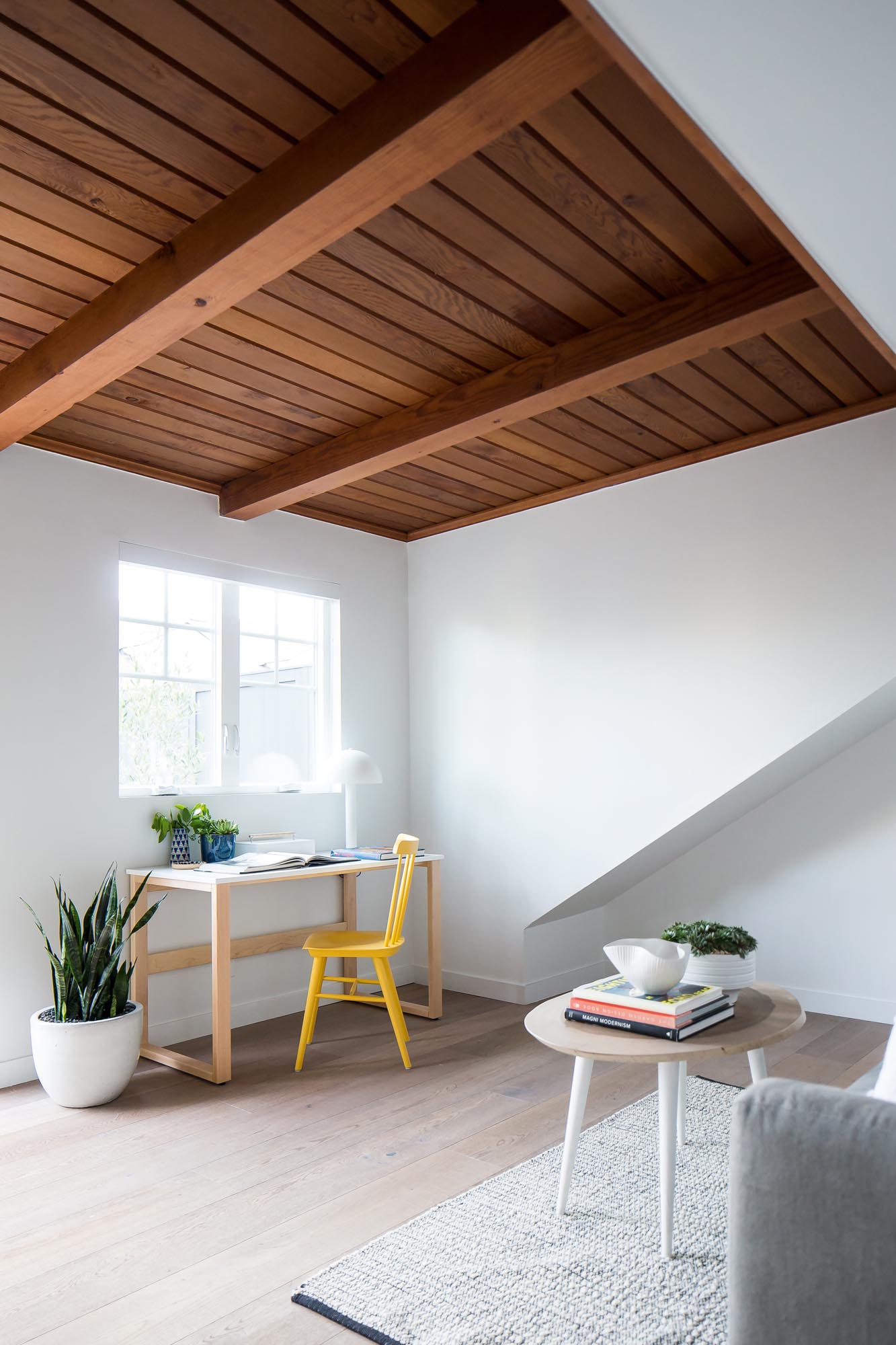 Photo of wood paneling on the ceiling with white walls and pale wood floor.