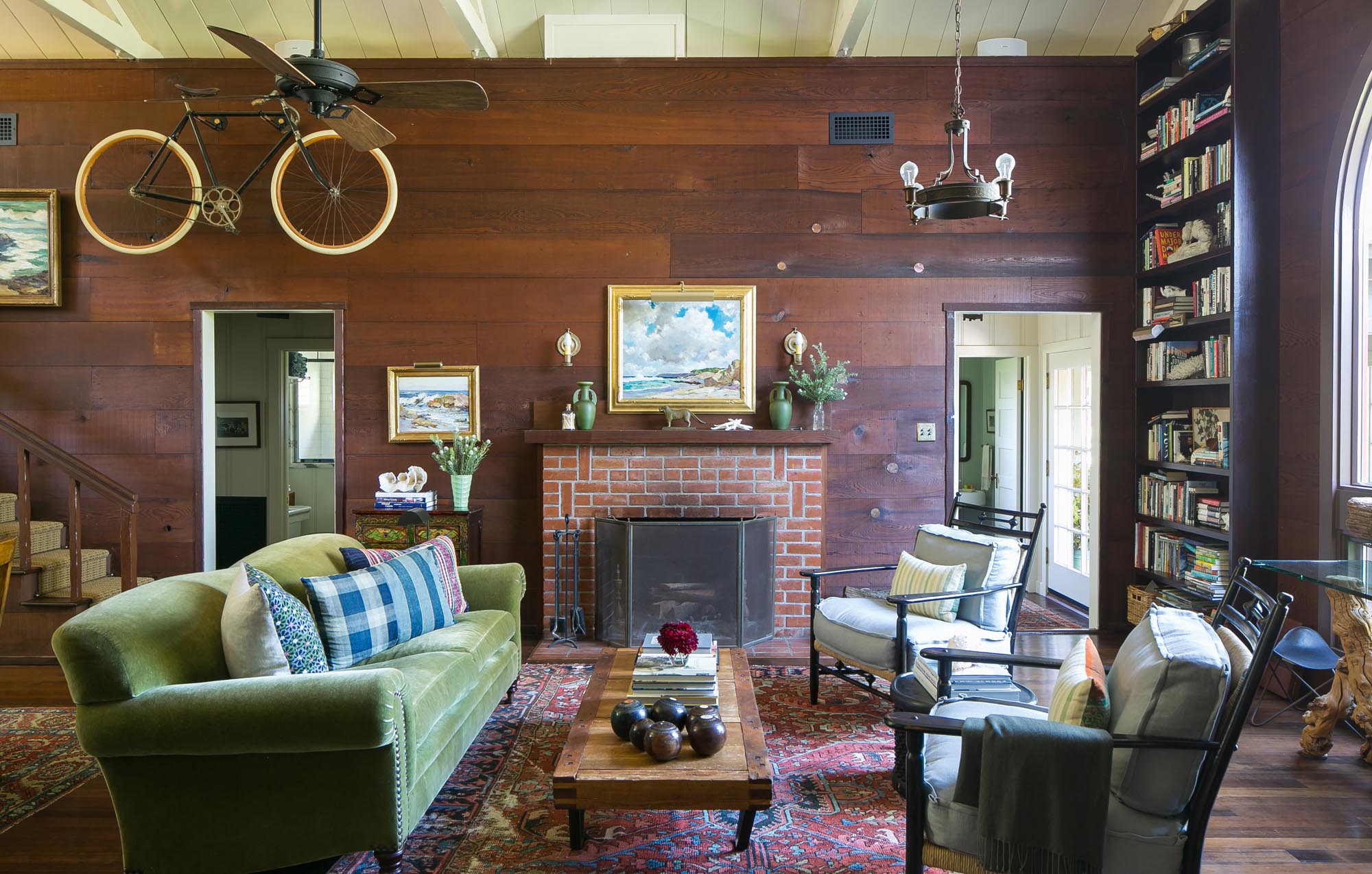 Photo of sitting area with wood-paneled walls decorated with paintings, a vintage bicycle, and tall bookshelves.