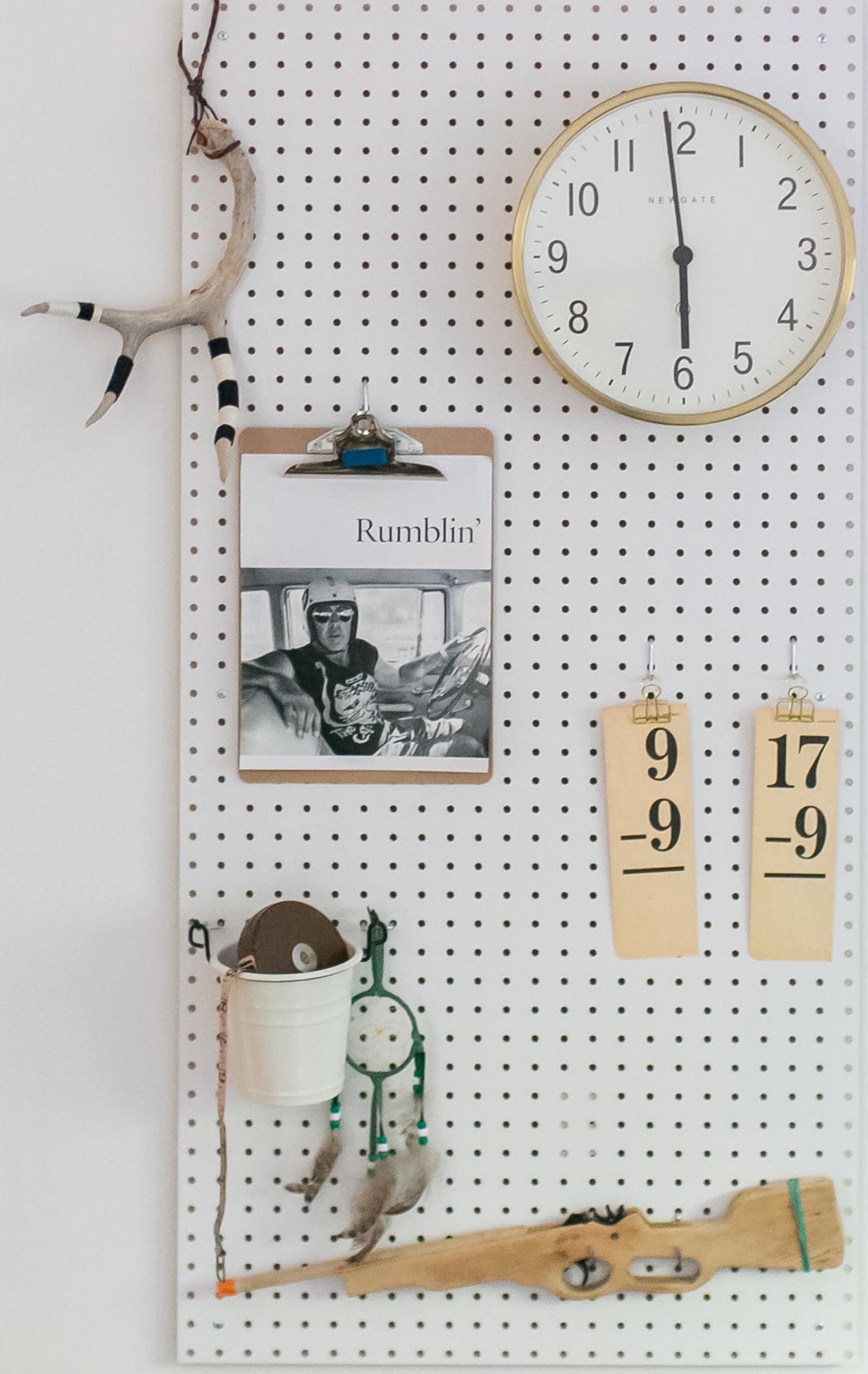 Photo of a pegboard with a clock, painted antler, flash cards, and a wooden toy rifle.