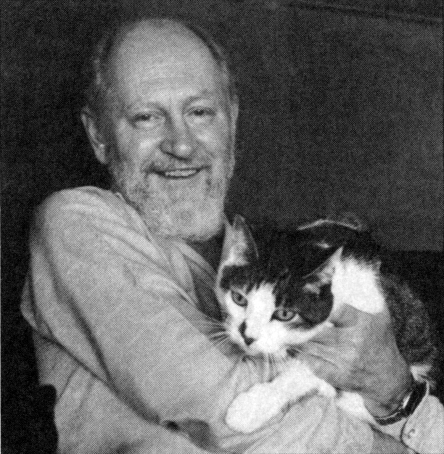 F. M. Busby is shown facing the camera, smiling happily and holding a tabby and white cat.