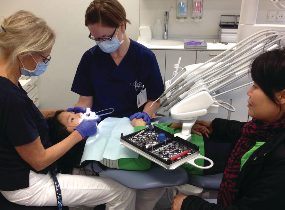 Photo displaying an assistant holding the patient’s right hand and head while the dentist is injecting the anesthesia.