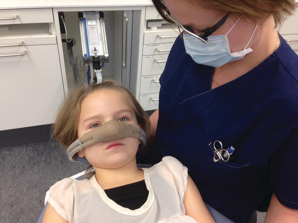 Photo displaying a young girl wearing nasal mask lying in supine position, held by a woman.