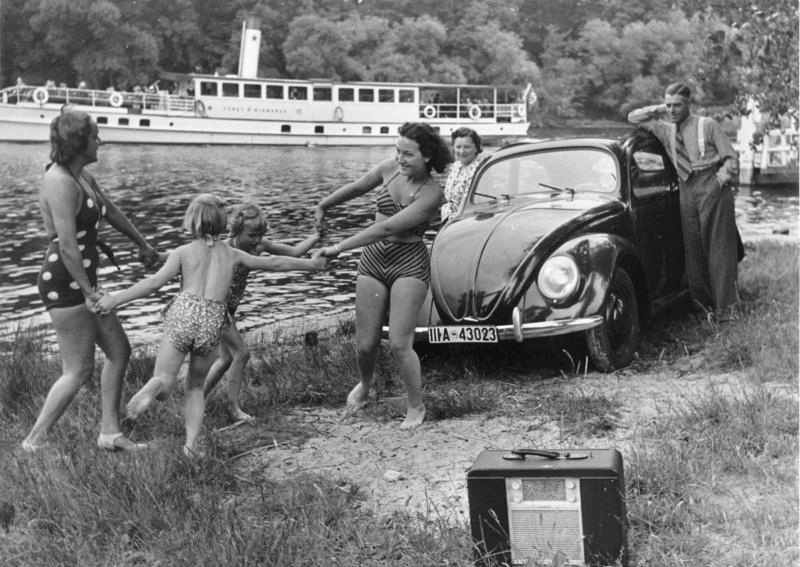 Vintage black and white photograph of a family playing in front of a Beetle