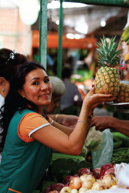 Photo showing a woman holding a pineapple in her hands and smiling at the viewer.