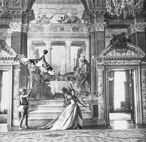 Mrs. Reginald Fellowes wearing a Dior gown and James Caffery holding parasol inside the Palazzo Labia's Tiepolo room, in Venice. (Photo by Cecil Beaton/Condé Nast via Getty Images)