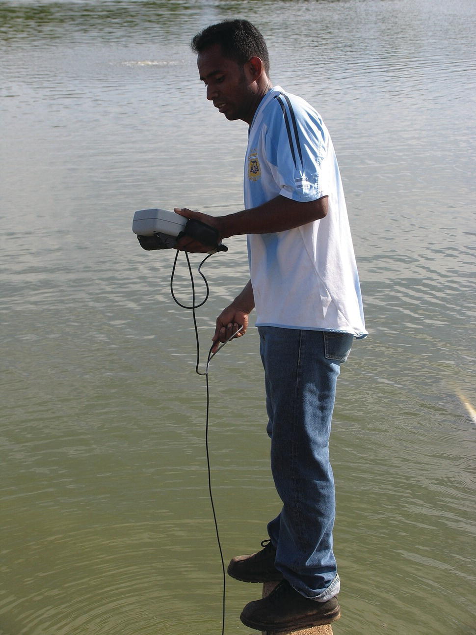 A man standing on a plank above the pond with oxygen meter in hand and DO probe down in the water column.