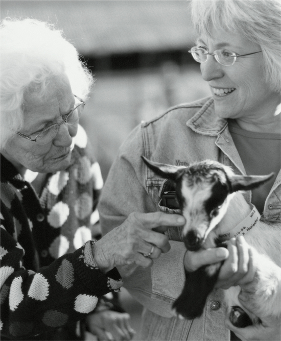 Cindy holding a baby goat while an elderly lady pets it