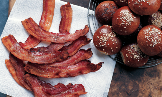 Crispy bacon on a paper towel and a wire basket full of rolls