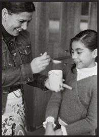 Making chocolate sauce and an older woman offering a spoon from a glass to a younger