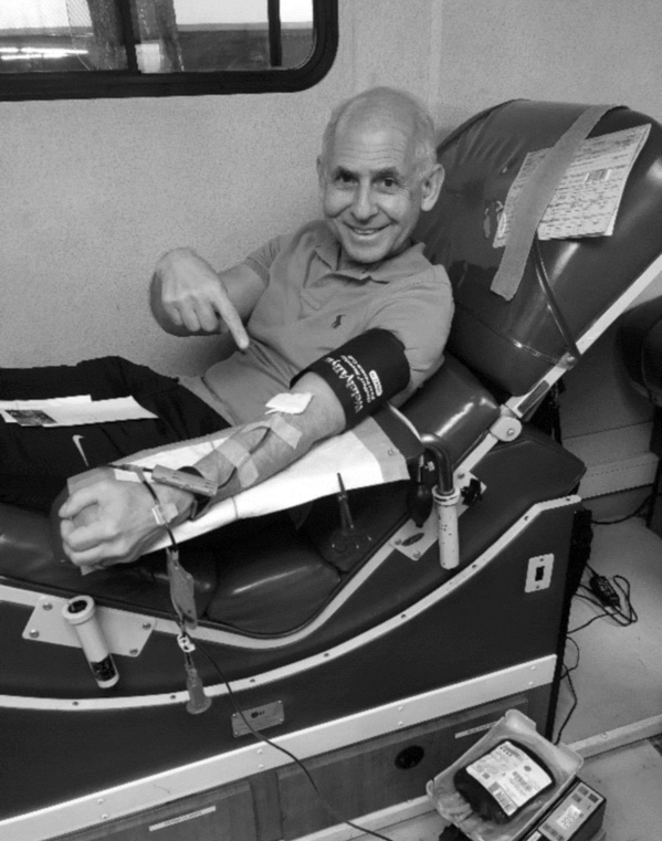 Dr. Amen sitting in a hospital chair, smiling and pointing at the IV in his arm.