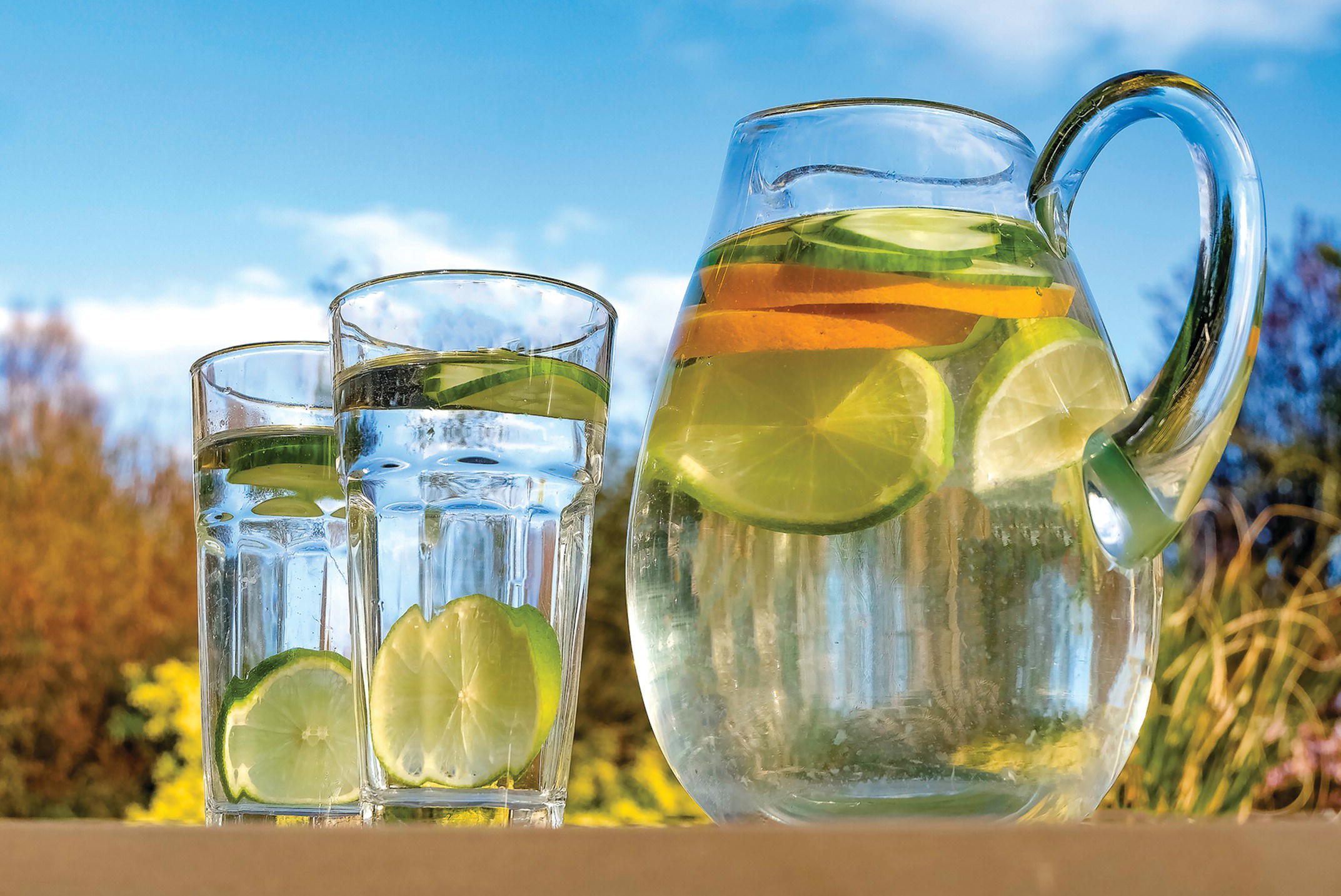 Photo displaying a pitcher of water with slices of limes and oranges and two glasses of water with slices of limes.