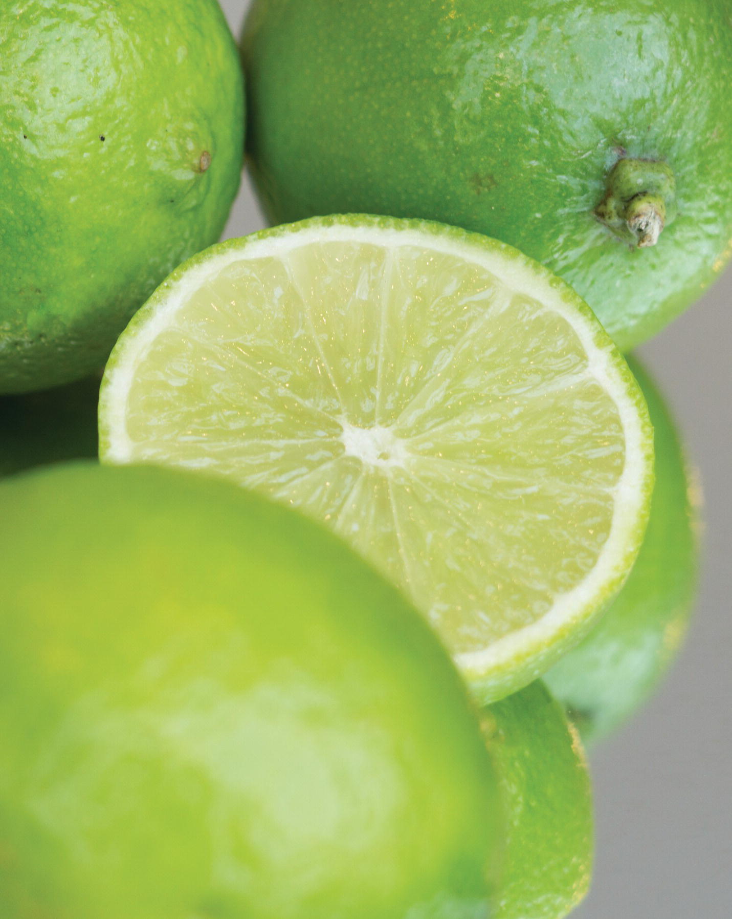 Photo displaying a slice of lime surrounded by three whole limes.