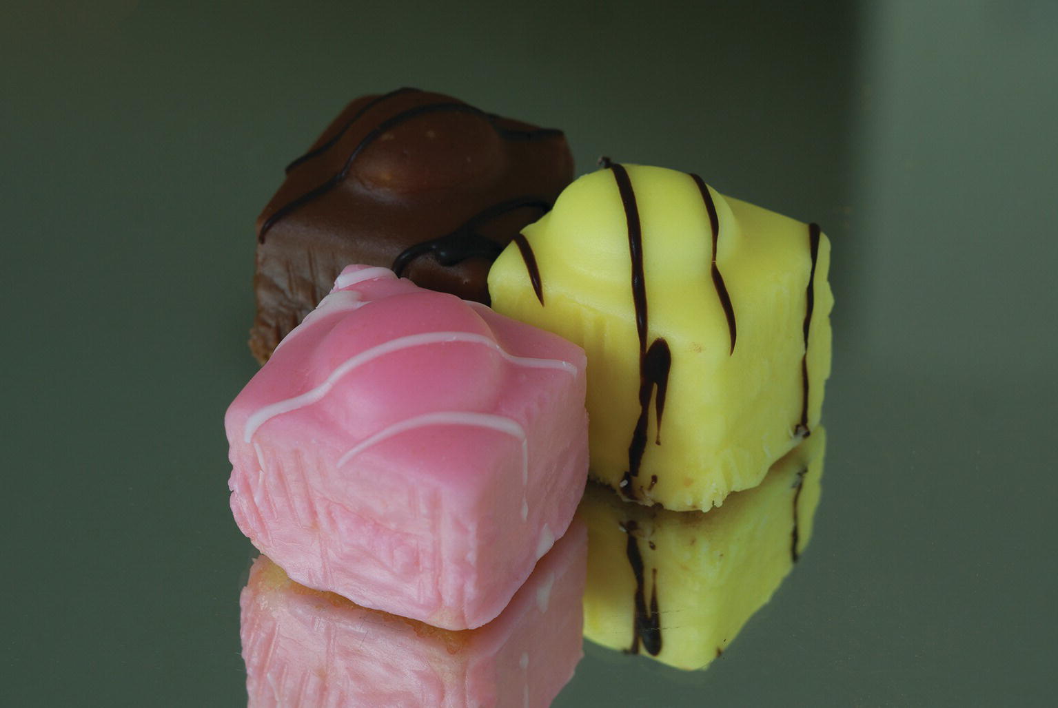 Photo displaying three cuboidal-shaped sweet treats in three various colors.