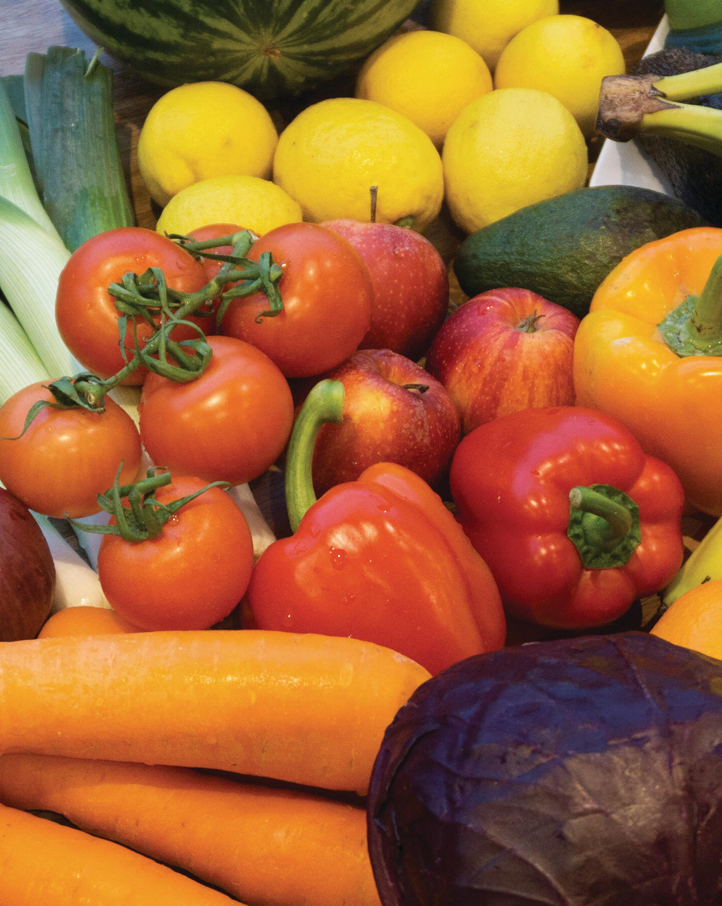 Photo displaying carrots, a purple cabbage, bell peppers, tomatoes, apples, avocado, spring onions, and lemons.