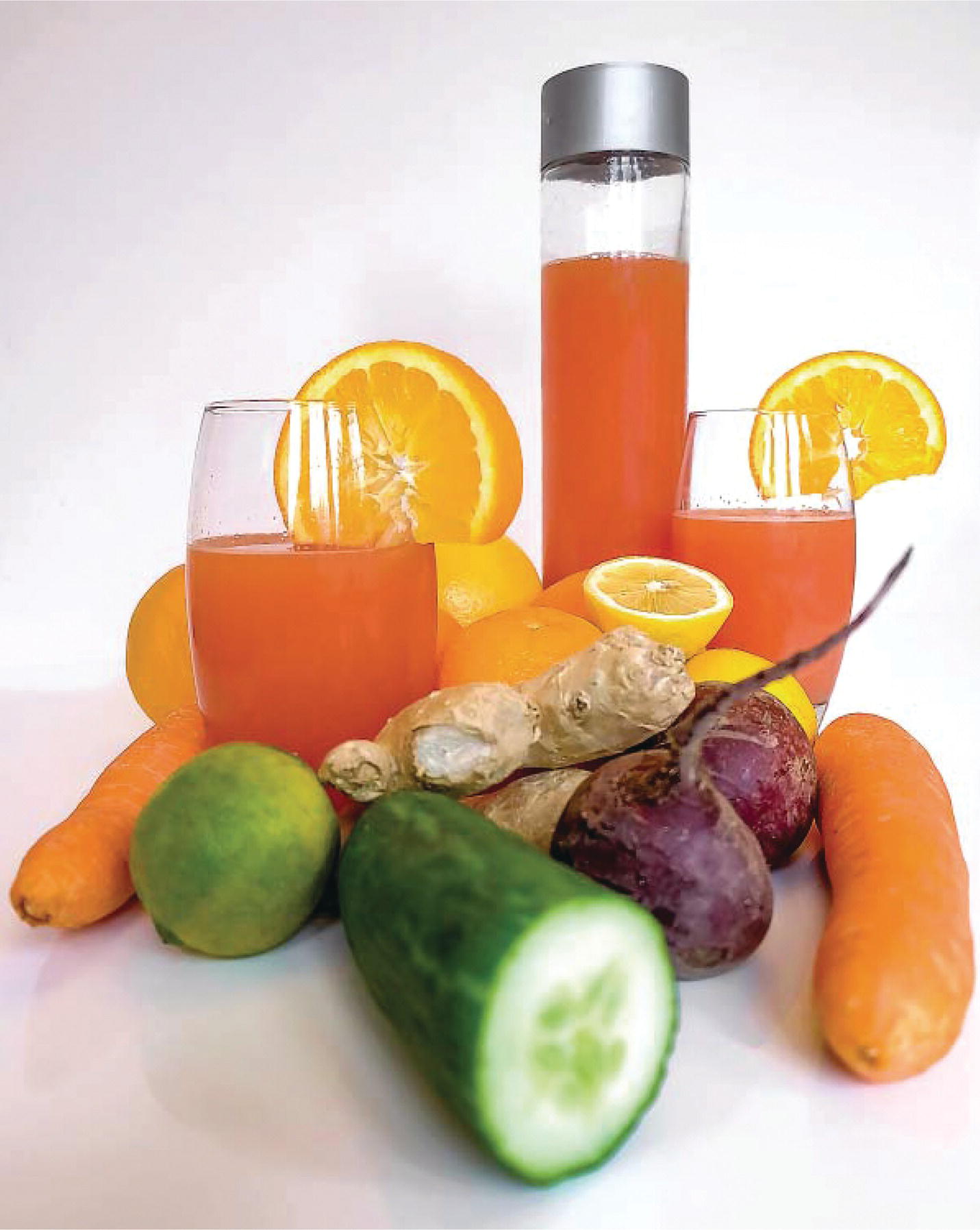 Photo displaying carrots, ginger, beetroots, cucumber, oranges, and glasses filled with orange juice.