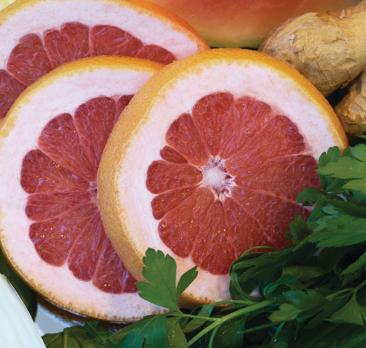 Photo displaying sliced pink grapefruit and parsley leaves.