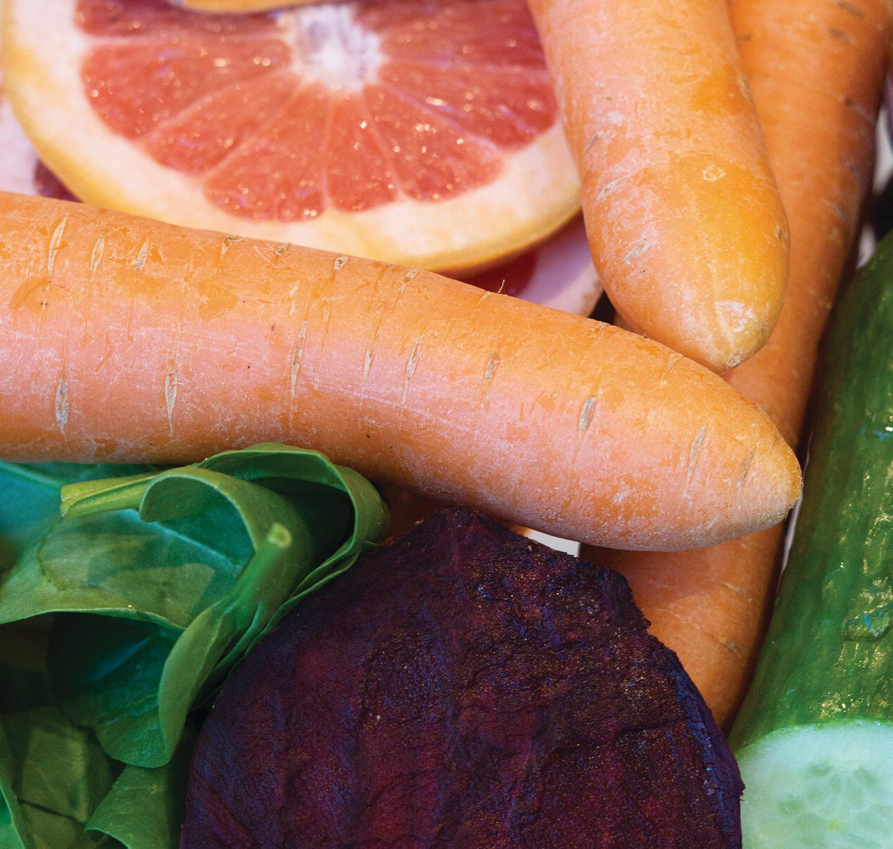 Photo displaying carrots, sliced pink grapefruit, spinach, and cucumber.