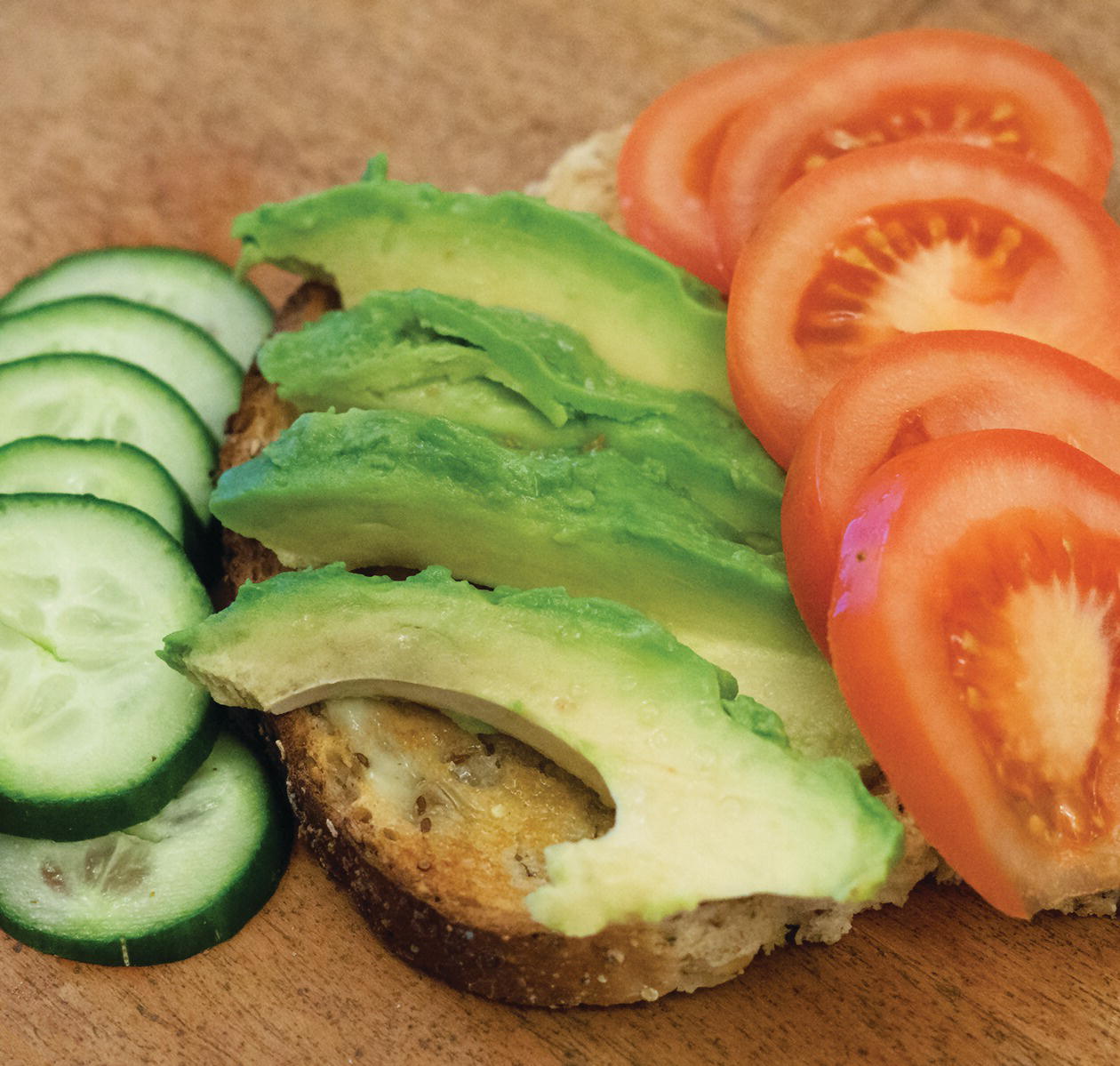 Photo displaying slices of avocado, slices of tomato, slices of cucumber, and a slice of lightly toasted bread.