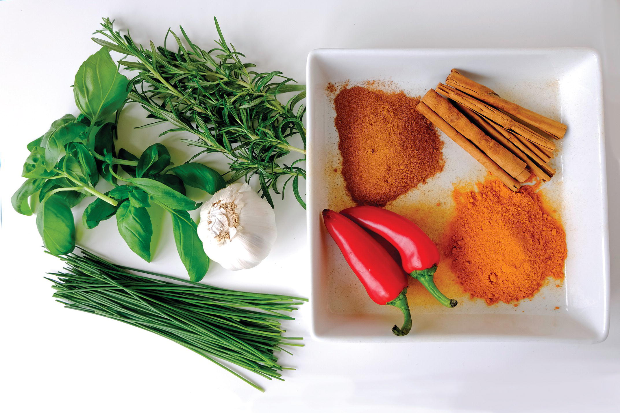 Photo displaying various spices and herbs such as chili peppers, cinnamon rolls and powder, rosemary, and turmeric powder.