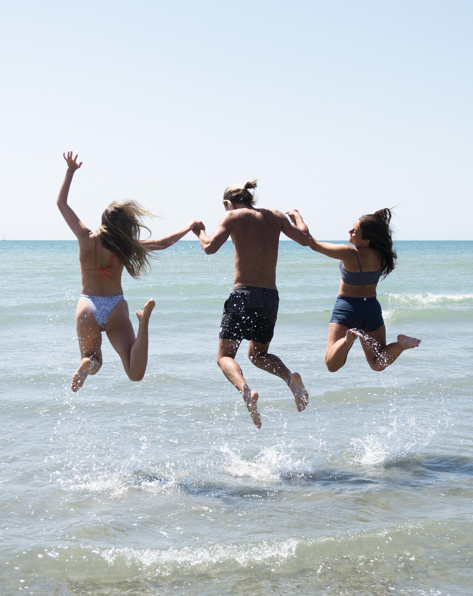 Photo displaying a man and two women jumping on the beach.