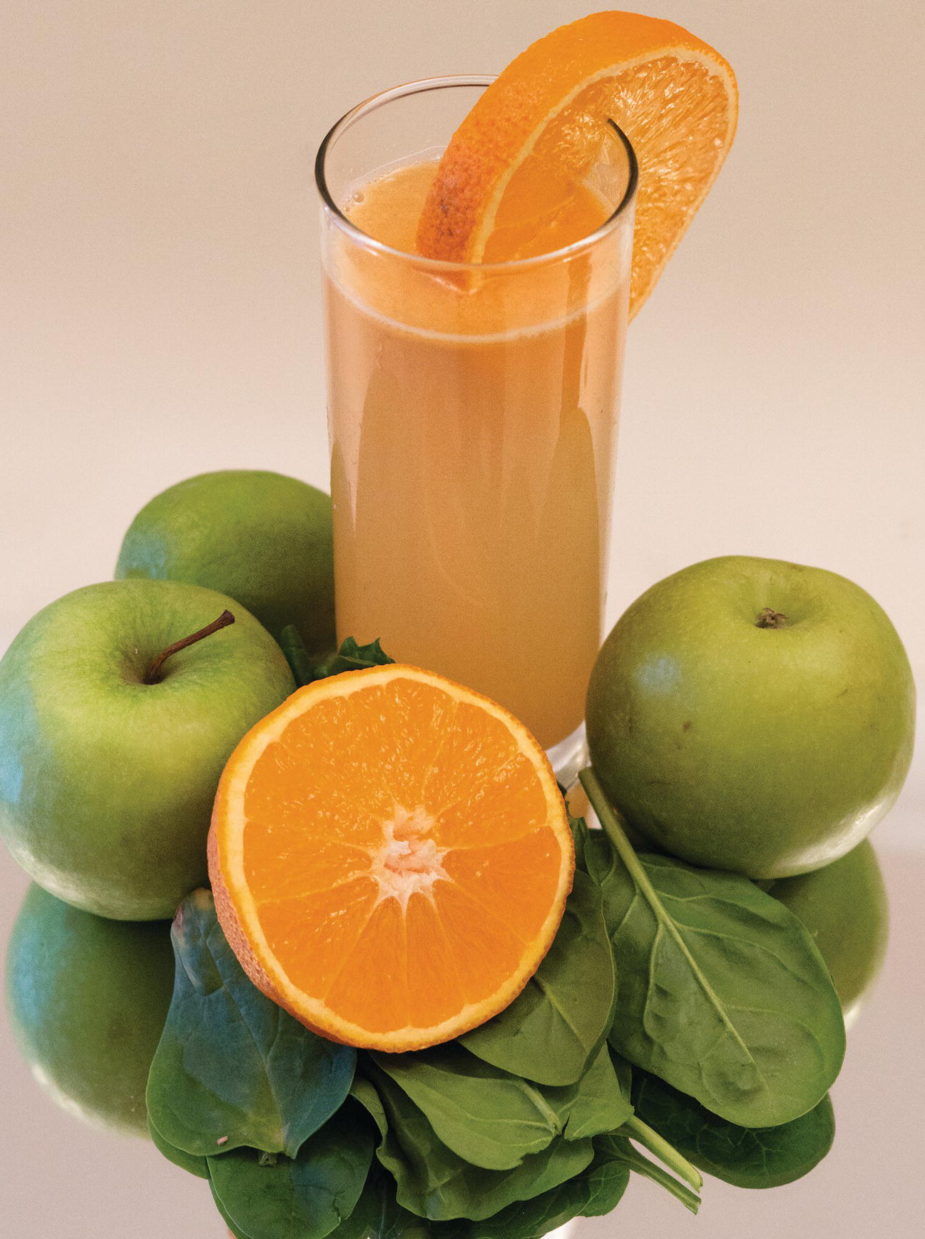 Photo displaying a sliced orange, spinach, a lime, two green apples, and a glass of juice.