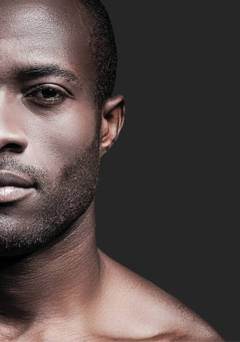 Half face of confident young African man looking at camera while standing against grey background