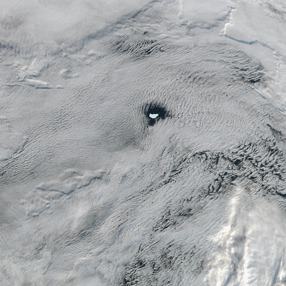 In June 2016, the Suomi NPP satellite captured this image of various cloud formations in the South Atlantic Ocean. Note how low stratus clouds framed a hole over iceberg A-56 as it drifted across the sea.  The exact reason for the hole in the clouds is somewhat of a mystery. It could have formed by chance, although imagery from the days before and after this date suggest something else was at work. It could be that the relatively unobstructed path of the clouds over the ocean surface was interrupted by thermal instability created by the iceberg. In other words, if an obstacle is big enough,  it can divert the low-level atmospheric flow of air around it, a phenomenon often caused by islands.