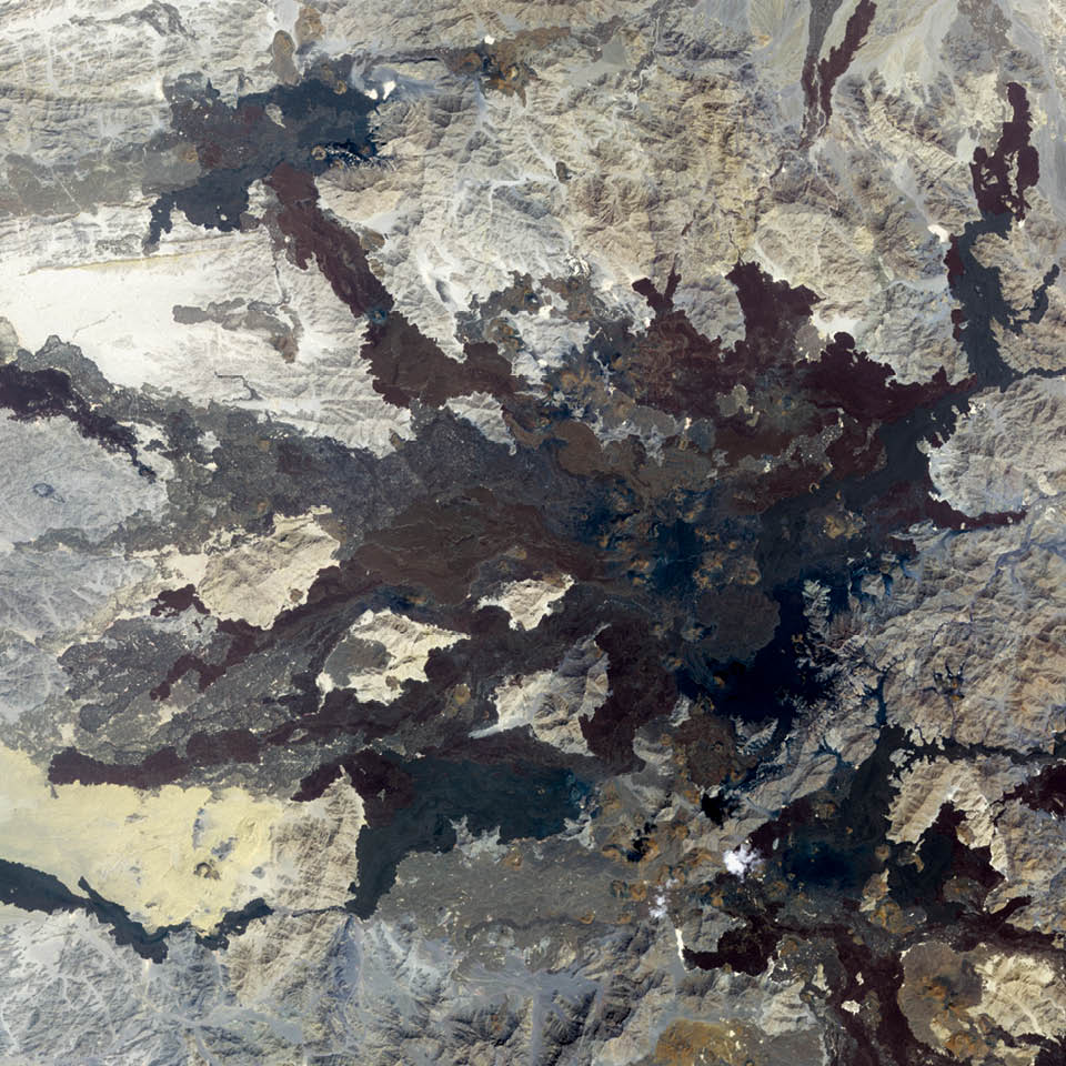 In northwestern Saudi Arabia lies a field of volcanic lava. Known as Harratt Lunayyir, the lava field contains some 50 cones from volcanic eruptions over the past 10,000 years. The Terra satellite captured this false-color image in October 2006. Old lava flows appear as irregular, dark stains on an otherwise light-colored landscape. Like ink on an uneven surface, the lava has formed rivulets of rock that flow out in all directions.