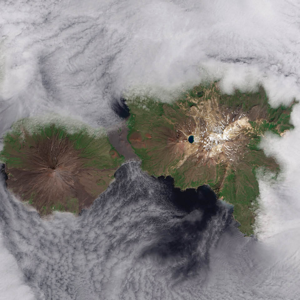 They are called the Islands of the Four Mountains. Part of the Aleutian Island chain, these peaks are actually the upper slopes of volcanoes rising from the seafloor: Carlisle, Cleveland, Herbert, and Tana. Standing in one of the most remote reaches of the world, these volcanoes have scarcely been studied. Satellite sensing makes that easier, as this Landsat 8 image from June 2013 shows. Herbert Island (right) is dominated by a symmetrical stratovolcano that stands in its center. The remote island has scarcely been studied, and there are no records of eruptions there. The 2-kilometer-wide summit caldera include a lake of meltwater, remnants of the snow that covers the peak for most of the year. The straight-down (nadir) satellite view can make it difficult to determine which part of the landscape stands taller than the other, a phenomenon known as relief inversion.