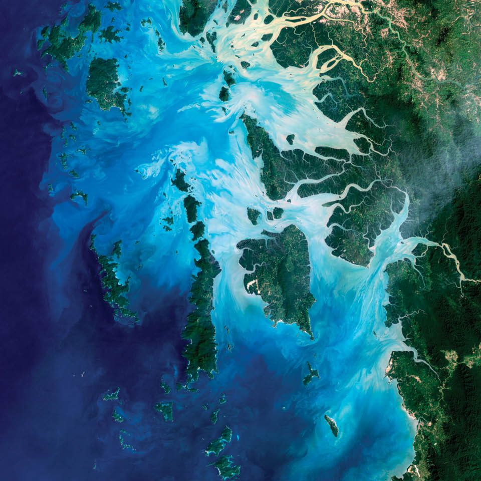 Near the border of Burma (Myanmar) and Thailand, more than 800 islands rise amid extensive coral reefs in the Andaman Sea.  This is the Mergui Archipelago.  In this view of Auckland Bay and Whale Bay, white swirling patterns in the near-shore waters are sediments that are carried out  by rivers and deposited on the seafloor. 