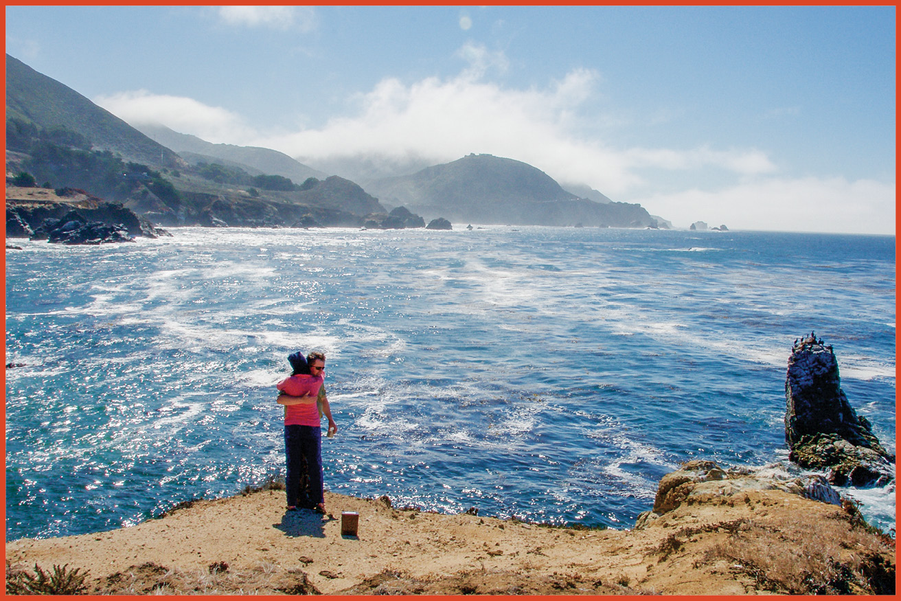 image of a man and woman hugging on a cliff next to the ocean