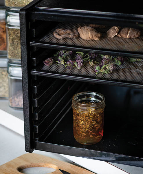 Mushrooms, flowers, and a jar of herbs in a large dehydrator.