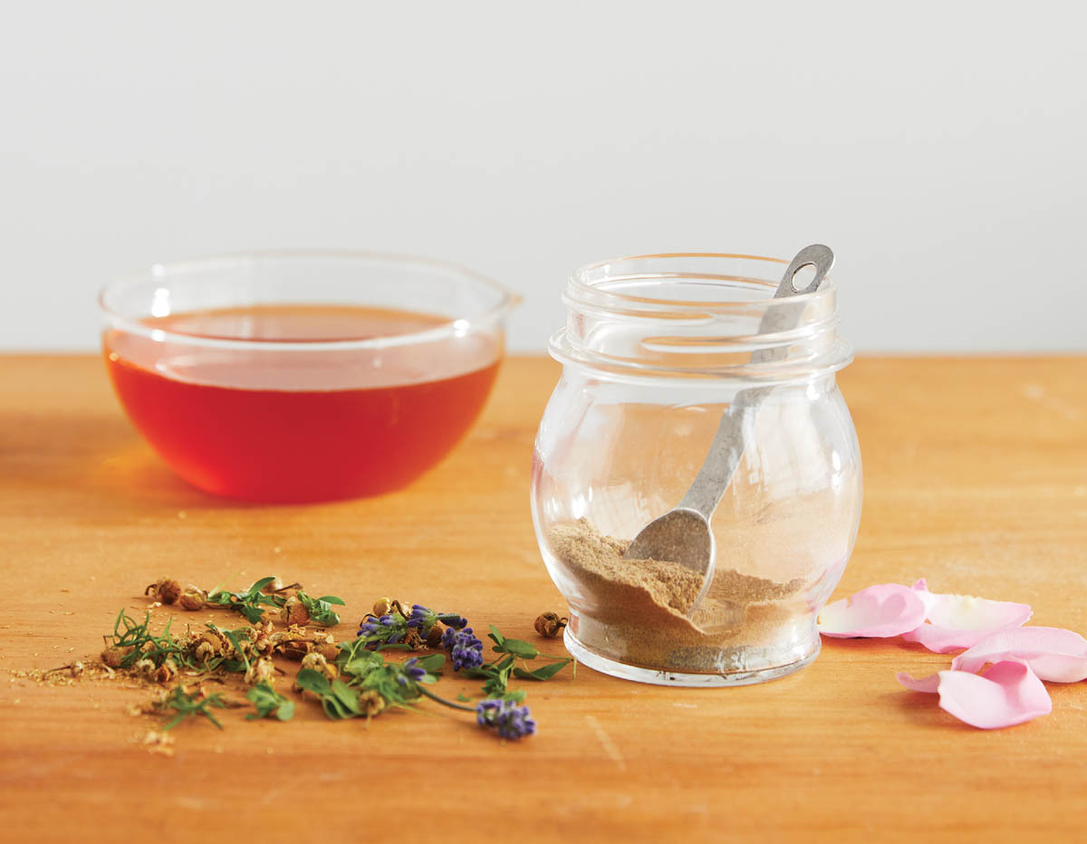 A dish of honey with a jar of seasoning and flower petals.